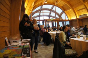 Attendees sitting down for our first breakfast together, while others drop off their gifts for the gift exchange and sign the map showing where they are from