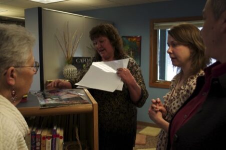 The Big Reveal: Carmella Hatch (right) presents DIBAJIMODAA — “Let’s Tell Stories” — posters featuring Red Cliff community members to tribal chair Rose Soulier (center) and TLAM mentor Louise Robbins (left).
